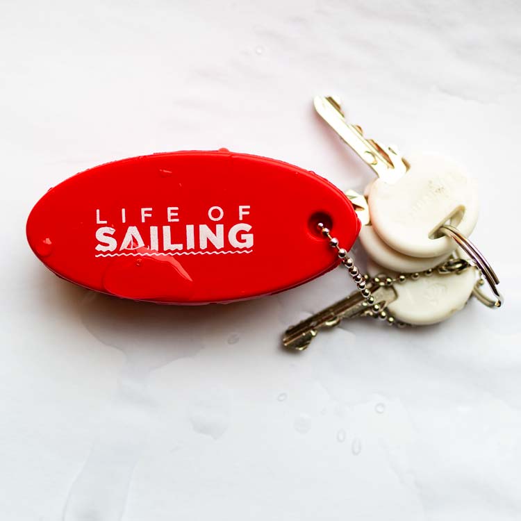 Floating keychain for sailing with 3 keys attached laying on a white background splashed with water